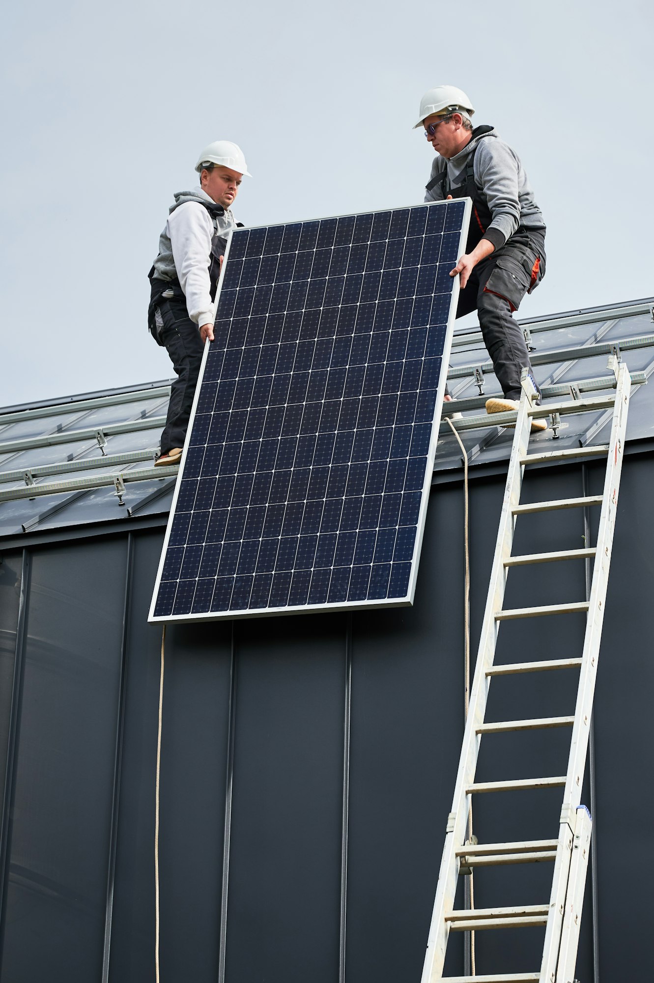 Workers lifting up photovoltaic solar module while installing solar panel system on roof of house.